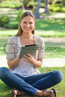 Smiling woman sitting on the lawn with her tablet computer