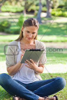 Woman sitting on the grass while using her tablet computer