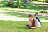 Smiling woman lying on the lawn with a tablet computer