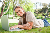 Smiling woman lying on the lawn with her laptop
