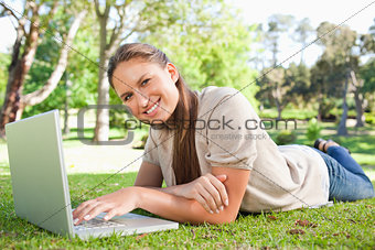 Smiling woman lying on the lawn with her laptop