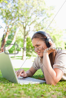 Woman with headphones and a laptop lying on the lawn