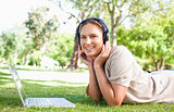 Woman with a laptop and headphones lying on the lawn