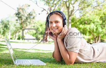 Woman with a laptop and headphones lying on the lawn