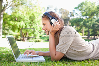 Side view of a woman with headphones and a laptop on the lawn