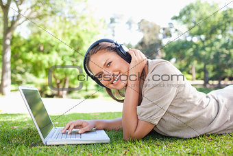 Side view of a smiling woman with headphones and a laptop lying 
