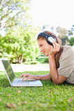 Side view of a woman with a laptop and headphones on the lawn