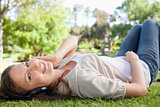 Smiling woman lying on the lawn while listening to music