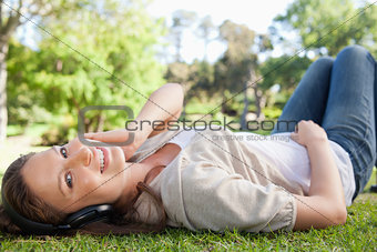 Smiling woman lying on the lawn while listening to music
