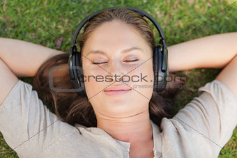 Relaxed woman lying on the lawn while listening to music