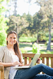 Smiling woman with her notebook on a park bench