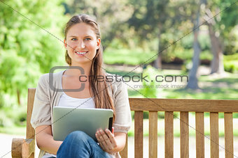 Smiling woman with a tablet computer on a park bench