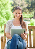 Smiling woman using a tablet computer on a park bench