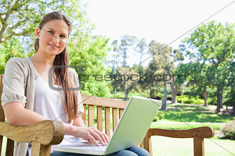 Smiling woman with a laptop on a park bench