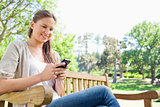 Smiling woman reading text message on a park bench