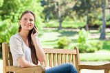 Smiling woman on her cellphone while sitting on a park bench