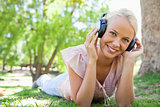 Smiling woman lying on the grass while listening to music