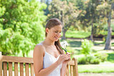 Smiling woman with a flower sitting on a park bench