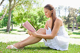 Side view of a woman sitting on the lawn while reading a book