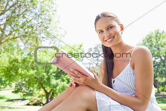 Side view of a smiling woman with a book on the lawn