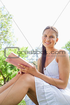 Side view of a smiling woman sitting in the park with a book