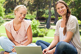 Smiling friends sitting in the park with a laptop