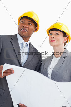 Smiling business people wearing hard hats are holding a paper