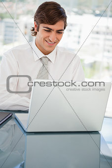 Smiling young businessman is on his laptop