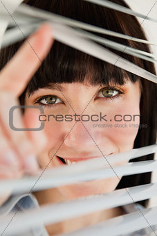 Close up of woman looking through blinds into the camera