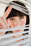A woman looking through some blinds into the camera