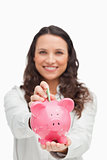 Portrait of a brunette putting money in the piggy bank