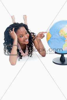 A young girl lying on the floor is pointing at a globe