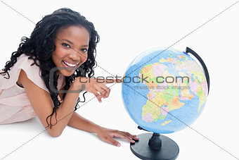 A young girl smiling at the camera has her finger on a globe