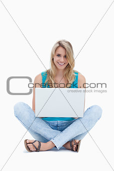 A young woman is sitting on the ground with a laptop