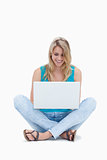 A woman is sitting on the ground looking at her laptop