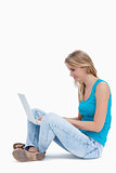 A side view of a woman sitting on the ground typing on a laptop 