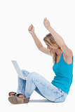 A woman has her arms in the air and a laptop between her legs