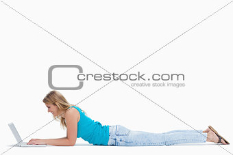 A woman is lying on the ground typing on her laptop