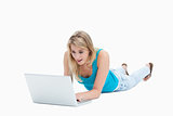 A surprised woman looking at a laptop is lying on the floor 