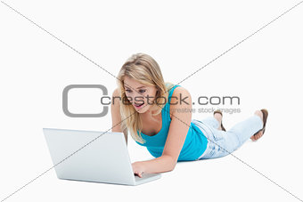 A surprised woman looking at a laptop is lying on the floor 