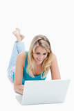 A smiling woman with a laptop is lying on the ground with her le