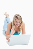 A woman with a laptop has her hand up and is lying on the floor 