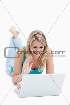 A woman with a laptop has her hand up and is lying on the floor 