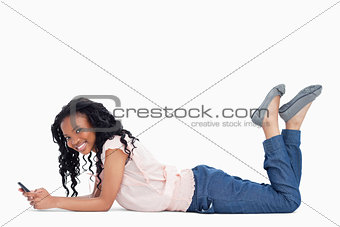 A young woman smiling at the camera is lying on the floor holdin