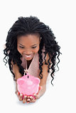 A smiling woman is looking at a piggy bank she is holding