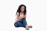 A smiling woman sitting on the floor is holding a mobile phone