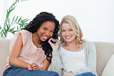 Two women listening to a mobile phone are smiling at the camera