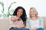 A woman with her friend is pointing a television remote control 