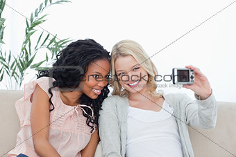 Two women are sitting down taking photo of themselves with a cam