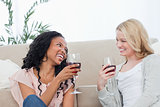 Two women sitting on the floor are talking and drinking wine